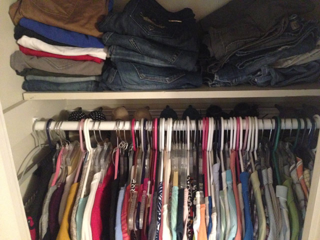 shirts hanging on closet rod with jeans folded on shelf above