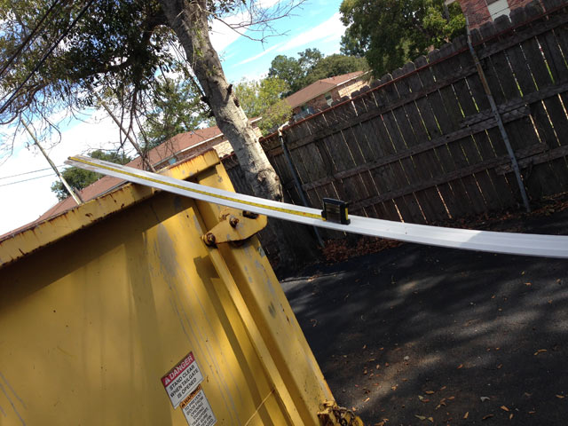 Long piece of white crown molding leaned against yellow dumpster