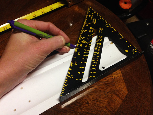 pen marking 45 degree angle on white crown molding with speed square