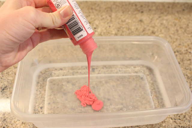 pouring pink acrylic paint into container of water