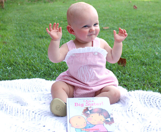 9 month old baby girl pose pink bubble outfit big sister book white blanket