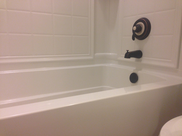 white bathtub with tile surround with brand new caulk sealant at joints