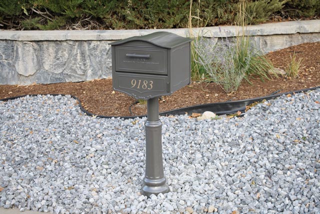designer mailbox installed in rock bed with gold numbers on front