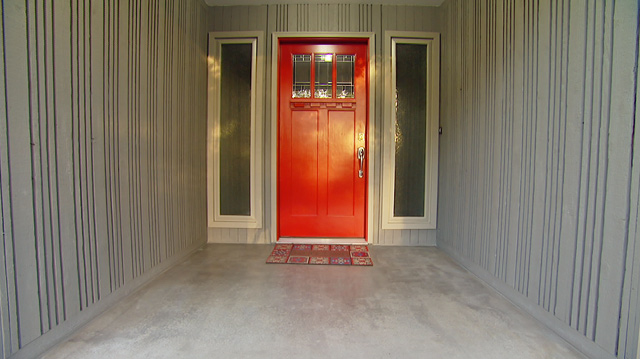 Red front door by grey concrete and porch