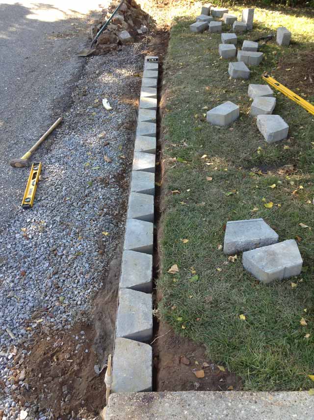laying gray concrete retaining wall blocks in straight line by green grass