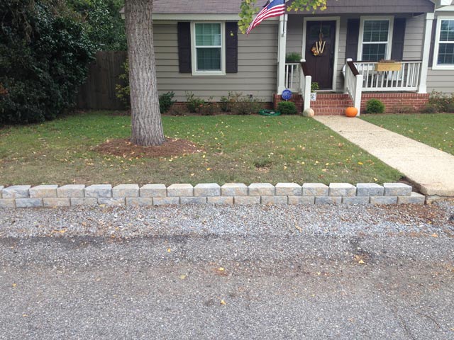 retaining wall on left side of front concrete walkway leading up to tan vinyl siding house with american flag