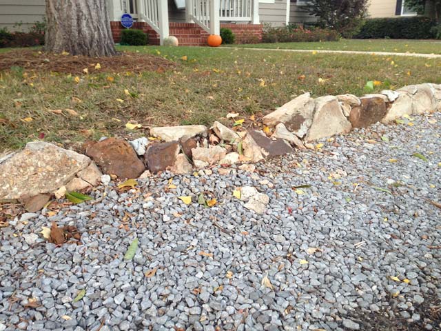 concrete retaining wall in bad shape with gravel and green grass around