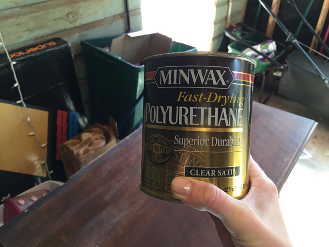hand holding can of clear satin polyurethane in front of wood dresser furniture in workshop