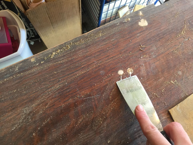 hand holding putty knife scraping paint stains off of wood stained dresser