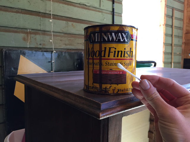 hand holding cotton swab in front of can of minwax wood stain