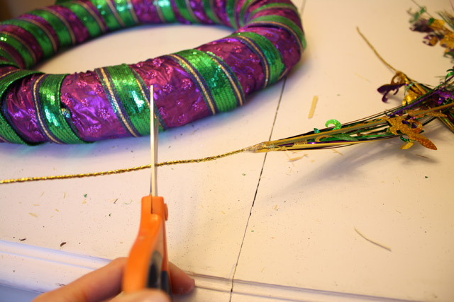 hand using scissors to cut Mardi Gras accent in front of purple gold and green wreath
