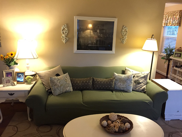 green slipcover on couch in yellow paint living room with sconces and framed poster on wall