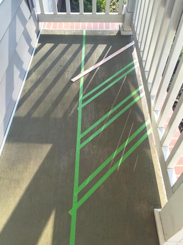 green painter's tape layout design on concrete porch with yardstick