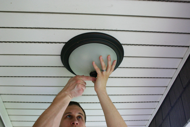 man hands removing flush mount light fixture from white vinyl porch ceiling