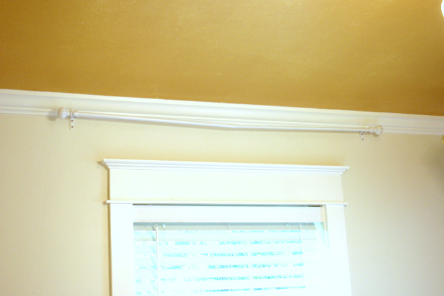 cream white walls with gold ceiling and white curtain rod dipping between brackets