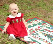 1 year old in Christmas dress posing for holiday card in grass on blanket