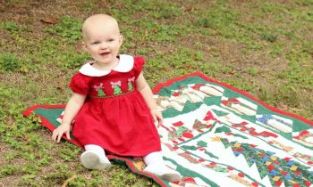 1 year old in Christmas dress posing for holiday card in grass on blanket